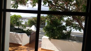 Blick durch ein Fenster auf einen Balkon mit weißer Wand, einer Holztür und einem gefliesten Boden.
