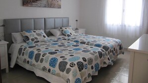 Ein Schlafzimmer mit einem Bett, einem Nachttisch, einer Lampe, einem Gemälde eines Leuchtturms und einem Fenster mit Vorhängen.