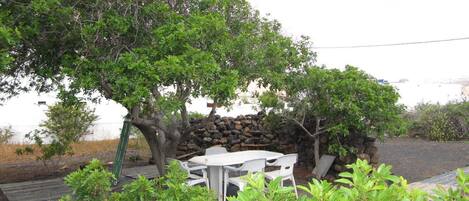 Un espace patio agrémenté d’un mur en pierre, d’une table avec des chaises et d’une végétation luxuriante.