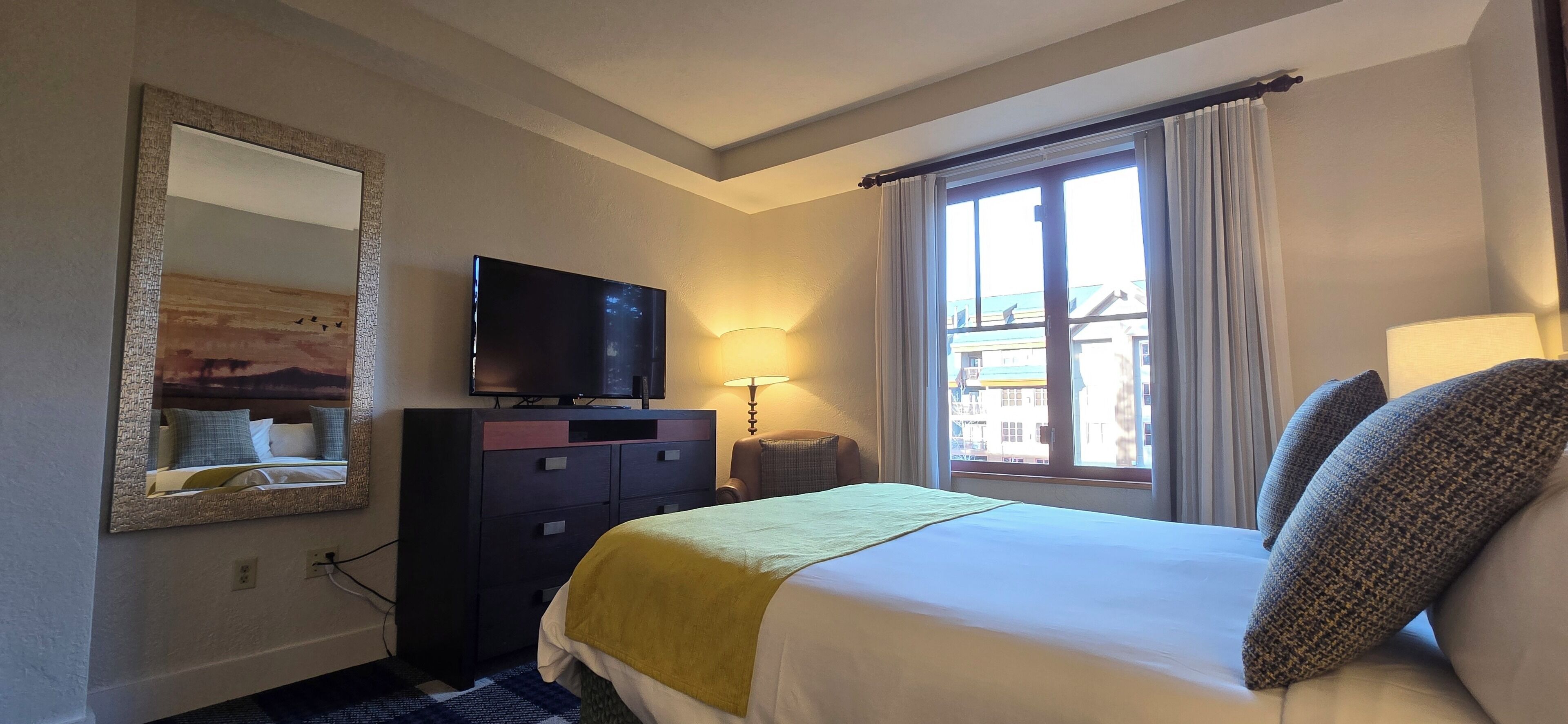 Una habitación de hotel con una cama, un televisor en una cómoda, una ventana con cortinas y una lámpara.