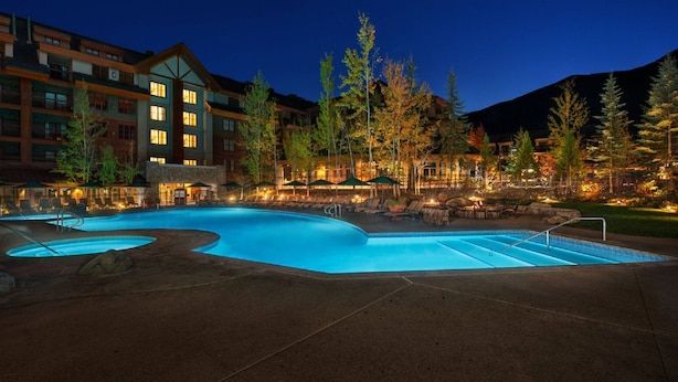 Un hotel con una amplia piscina exterior, numerosas habitaciones y un paisaje montañoso de fondo.