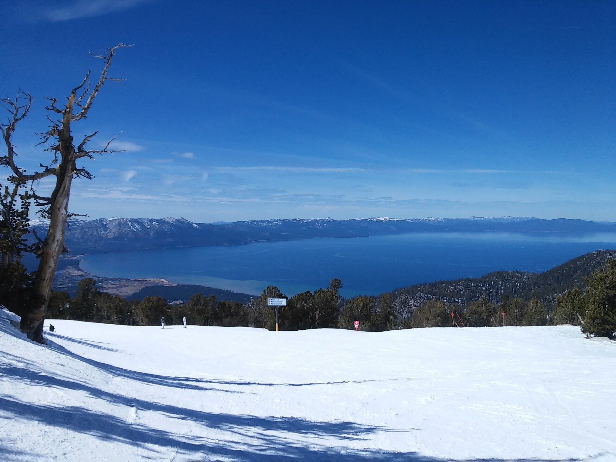 Pendiente nevada con vista despejada de un lago y montañas lejanas.