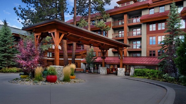 A multi-story hotel with a covered outdoor area, stone pillars, and a variety of plants.