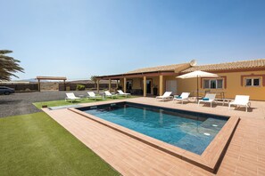 A swimming pool with lounge chairs and a pergola in a backyard setting.