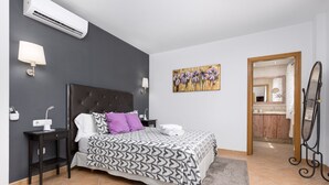 Een slaapkamer met een groot bed, een nachtkastje, een airconditioner en een schilderij aan de muur.