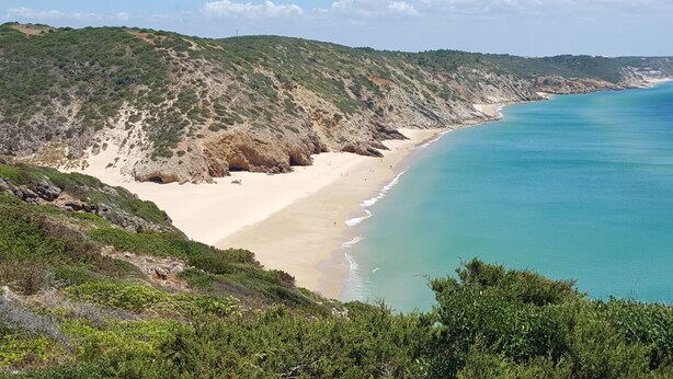 Eine Küstenlandschaft mit Sandstrand, Felsküste und blauem Meer.