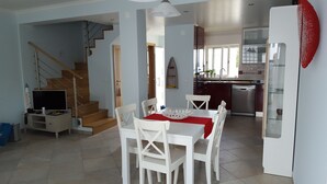 Eine moderne Küche mit Edelstahlgeräten, ein Essbereich mit weißen Stühlen und einer roten Tischdecke sowie eine Treppe, die in ein weiteres Geschoss führt.