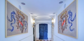 A hallway with checkered flooring, two ornate wall paintings, and a blue door at the end.