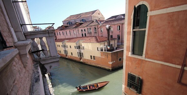 A narrow waterway with a boat, buildings on either side, and a balcony overlooking the scene.