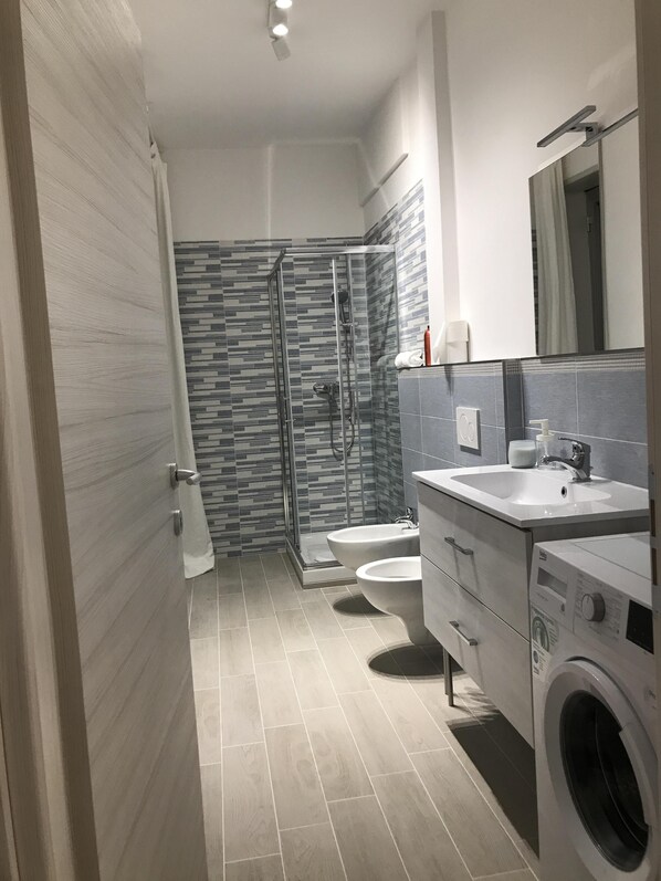 Une salle de bain moderne équipée d’une douche, de toilettes, d’un lavabo et d’un lave-linge.