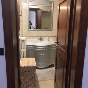 Une salle de bain avec un lavabo blanc, un miroir, une porte en bois et un radiateur.
