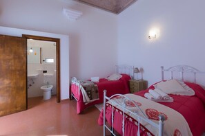 Une chambre avec deux lits, une porte en bois, une salle de bain avec un miroir et un luminaire fixé au mur.