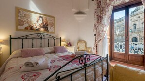 Un dormitorio con cama, un cuadro, una ventana que ofrece vistas a un edificio y una silla.