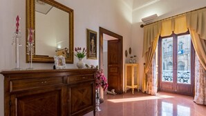 Una habitación con un armario de madera, un espejo, un jarrón con flores y una puerta que da a un espacio exterior con vistas a edificios.