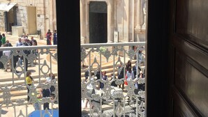 Vista desde un balcón sobre una plaza pública con arquitectura clásica, incluyendo columnas y detalles ornamentados.