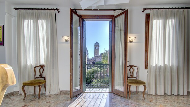 A room with a balcony, two chairs, and a view of a tower. - SUNNY Ghetto canal (Venezia)