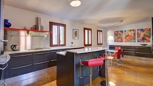 A modern kitchen with a central island, bar stools, and a view of the living area. - SUNNY Ghetto canal (Venezia)