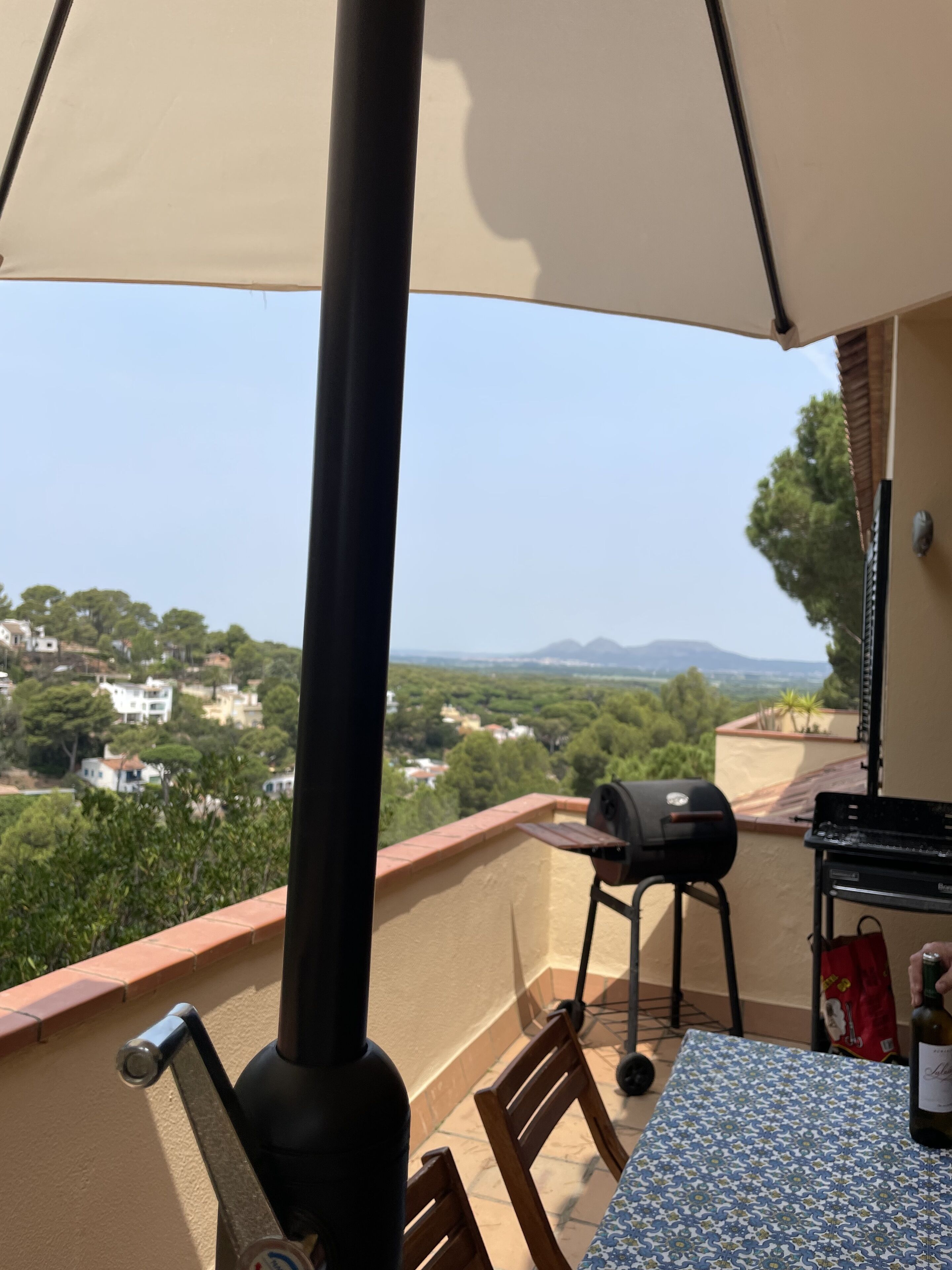 A balcony with a table, chairs, a grill, and a view of a town and mountains.