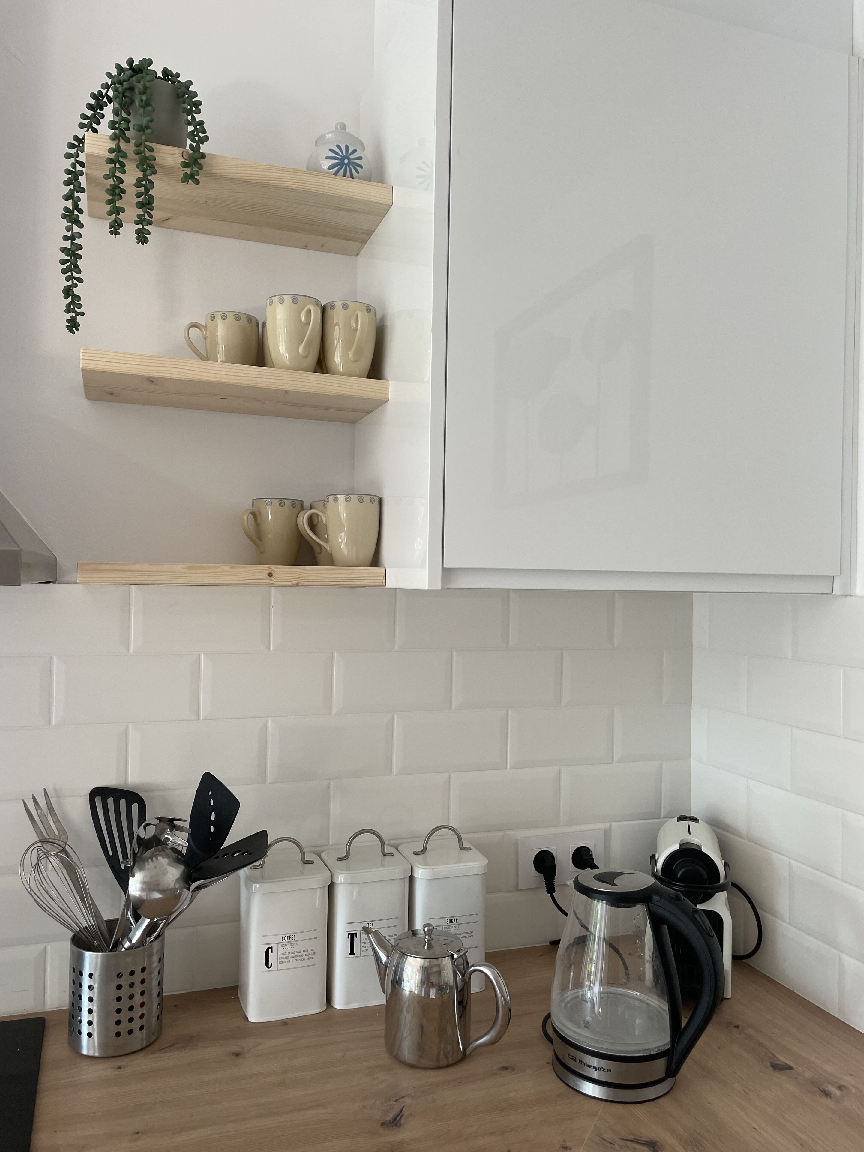 A kitchen with white cabinets, wooden shelves, and a coffee maker.