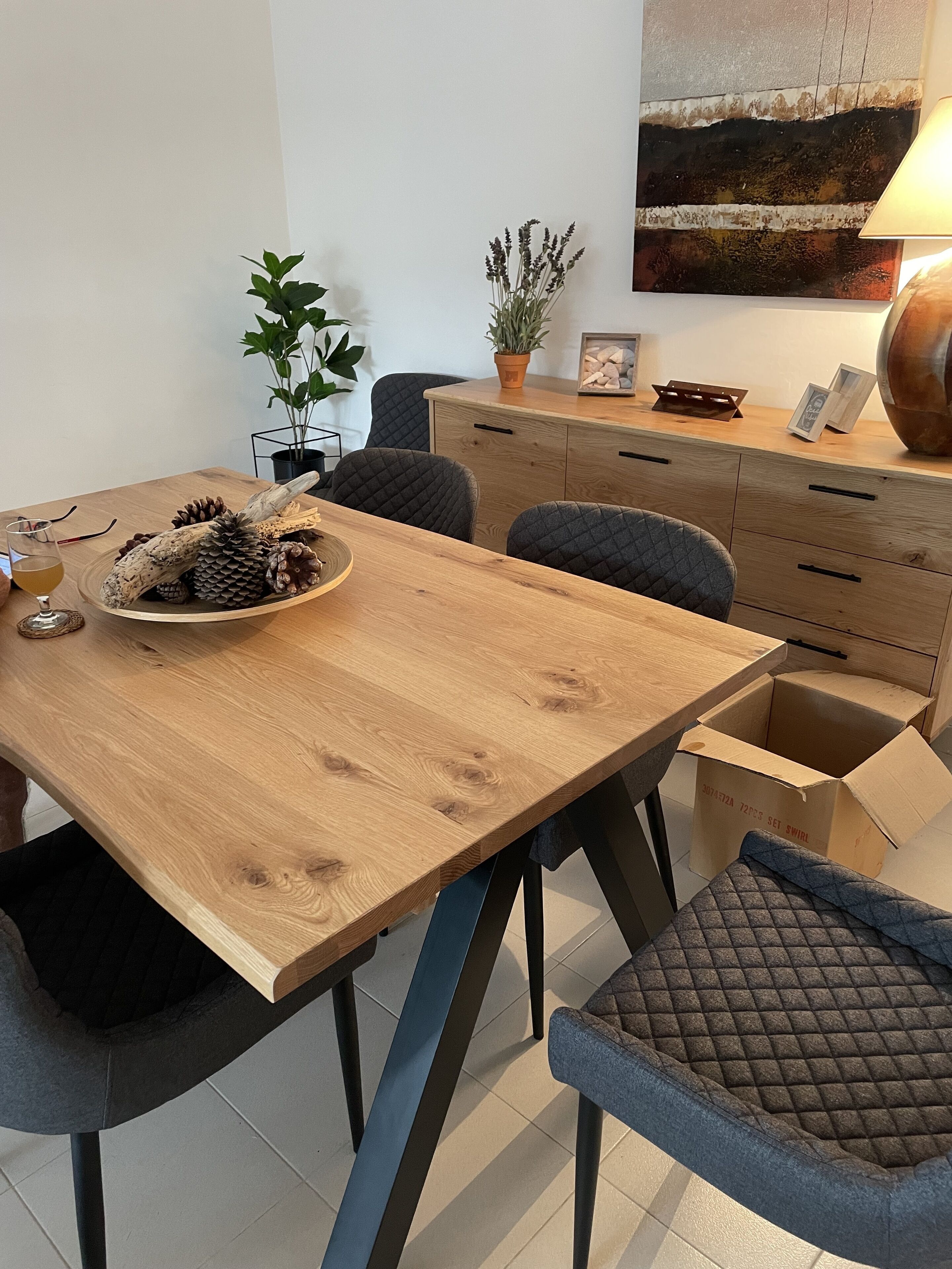 Una mesa de comedor de madera con un bol de piñas y una copa de vino, rodeada de sillas acolchadas.