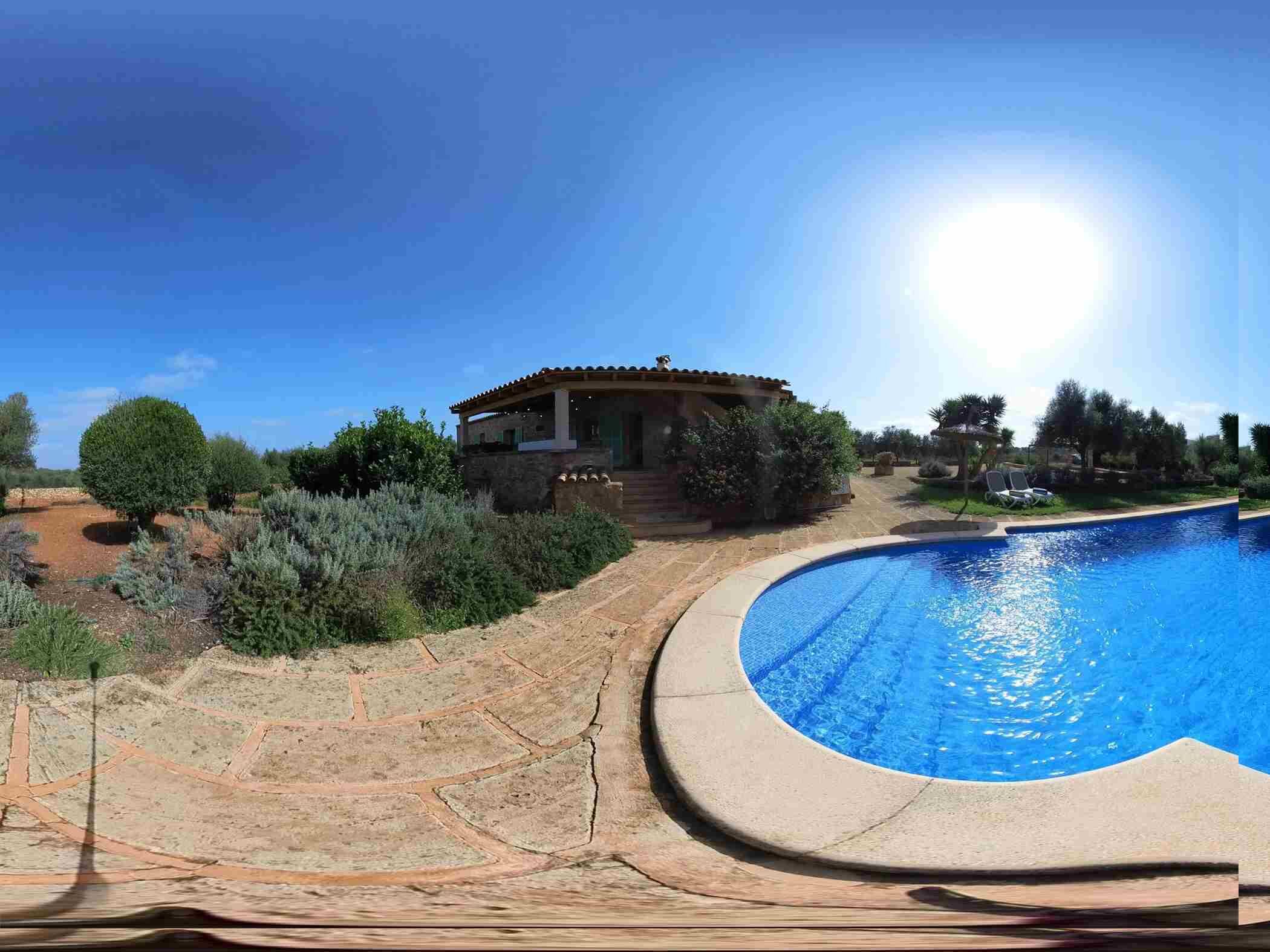 A house with a swimming pool, surrounded by dry vegetation and a clear sky.
