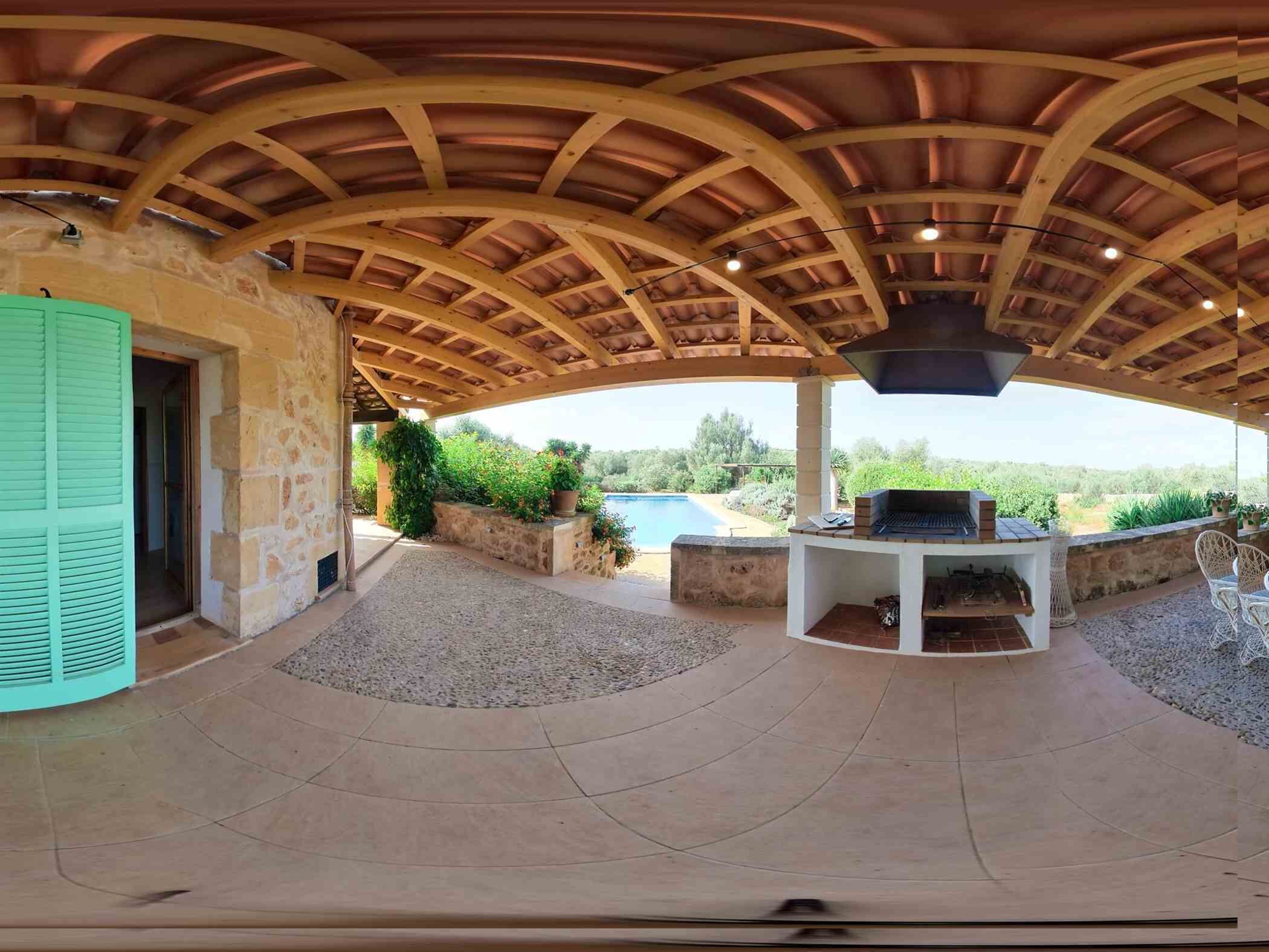 An outdoor patio with a stone wall, a grill, and a view of a swimming pool.