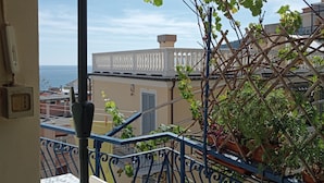 A balcony with a patterned table, a metal railing, and potted plants. - Apartment with sea view, 5 minutes from the beach (Finale Ligure)