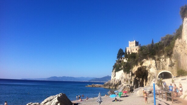 A beach with a castle on a cliff, clear blue sky, and the sea. - Apartment with sea view, 5 minutes from the beach (Finale Ligure)
