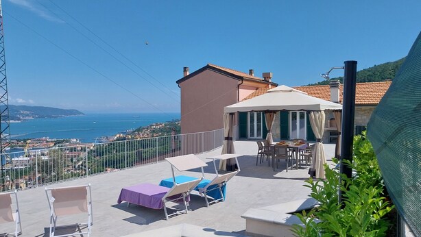 Eine Terrasse mit Sitzgelegenheiten im Freien, einem Tisch und Blick auf das Meer sowie entfernte Gebäude.
