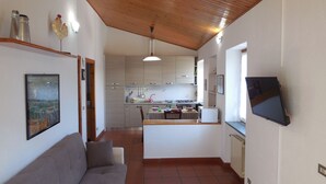 Eine moderne Küche mit weißen Schränken, ein Essbereich mit einer Couch und einem an der Wand montierten Fernseher.