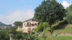 Une maison à deux étages dotée d’un balcon, entourée d’une végétation luxuriante et d’arbres.