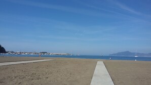 Une plage avec un ciel dégagé, une promenade en béton et des bateaux sur l’eau.