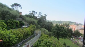 Une colline avec un mur de pierres et une clôture en métal. On aperçoit des arbres et des bâtiments au loin.