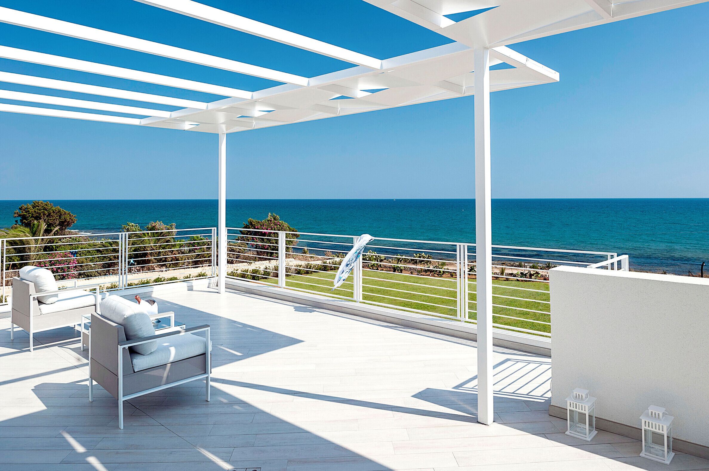 A terrace with white furniture, a view of the sea, and a clear sky.