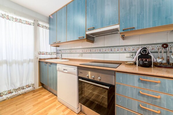 Een keuken met blauwe kastjes, een vaatwasser, een oven en een aanrecht met een waterkoker.