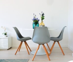 A dining area with a white table, three grey chairs with wooden legs, and a vase with flowers on the table.