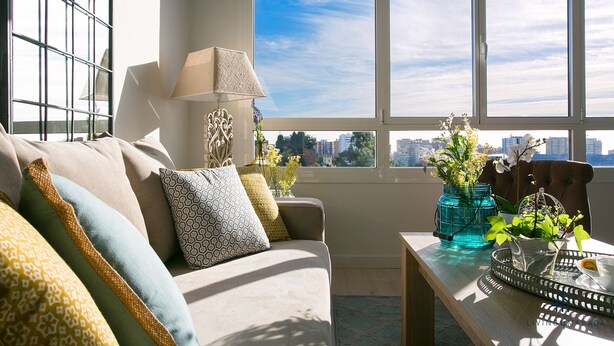A modern living room with a sofa, patterned cushions, a lamp, and a view of the city through large windows. - Alcazaba Exclusive View Living4malaga (Málaga)