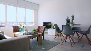 A modern living room with a dining area, large windows, a flat-screen TV, and a view of the city. - Alcazaba Exclusive View Living4malaga (Málaga)