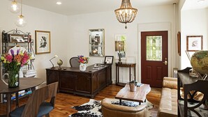 A spacious living room with a wooden floor, a leather sofa, a dining table with chairs, a desk with a globe and books, and a chandelier. - Moonriver Inn (Narrowsburg)