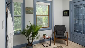 A room with three windows, a potted plant, a chair, a small table, and a rug. - Moonriver Inn (Narrowsburg)