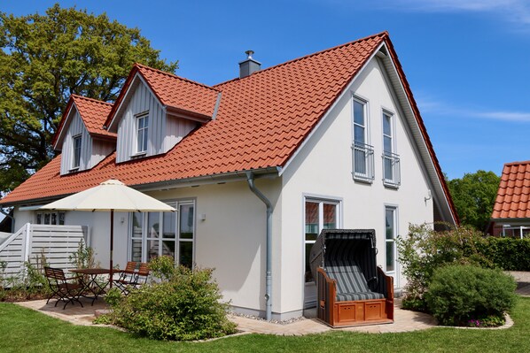 A two-story house with a red-tiled roof, white exterior walls, and a balcony with a wicker chair. - Semi-detached house " Seestern " on the Baltic Sea, fireplace, sauna, free WLAN -SEASIDE- (Rosenhagen)