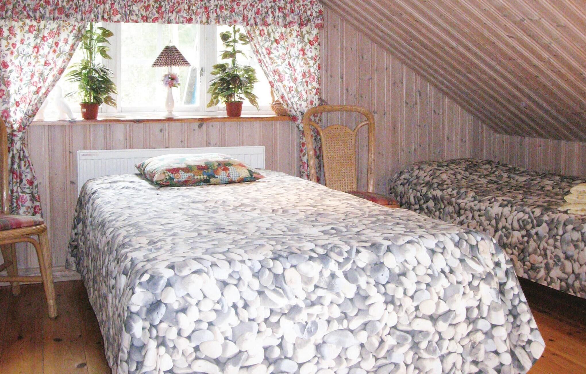 A bedroom with two beds, floral curtains, potted plants, a lamp, and a wooden chair.