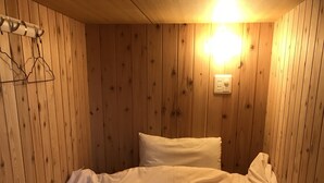Un lit simple avec une couette matelassée, des murs en bois et un luminaire fixé au mur.