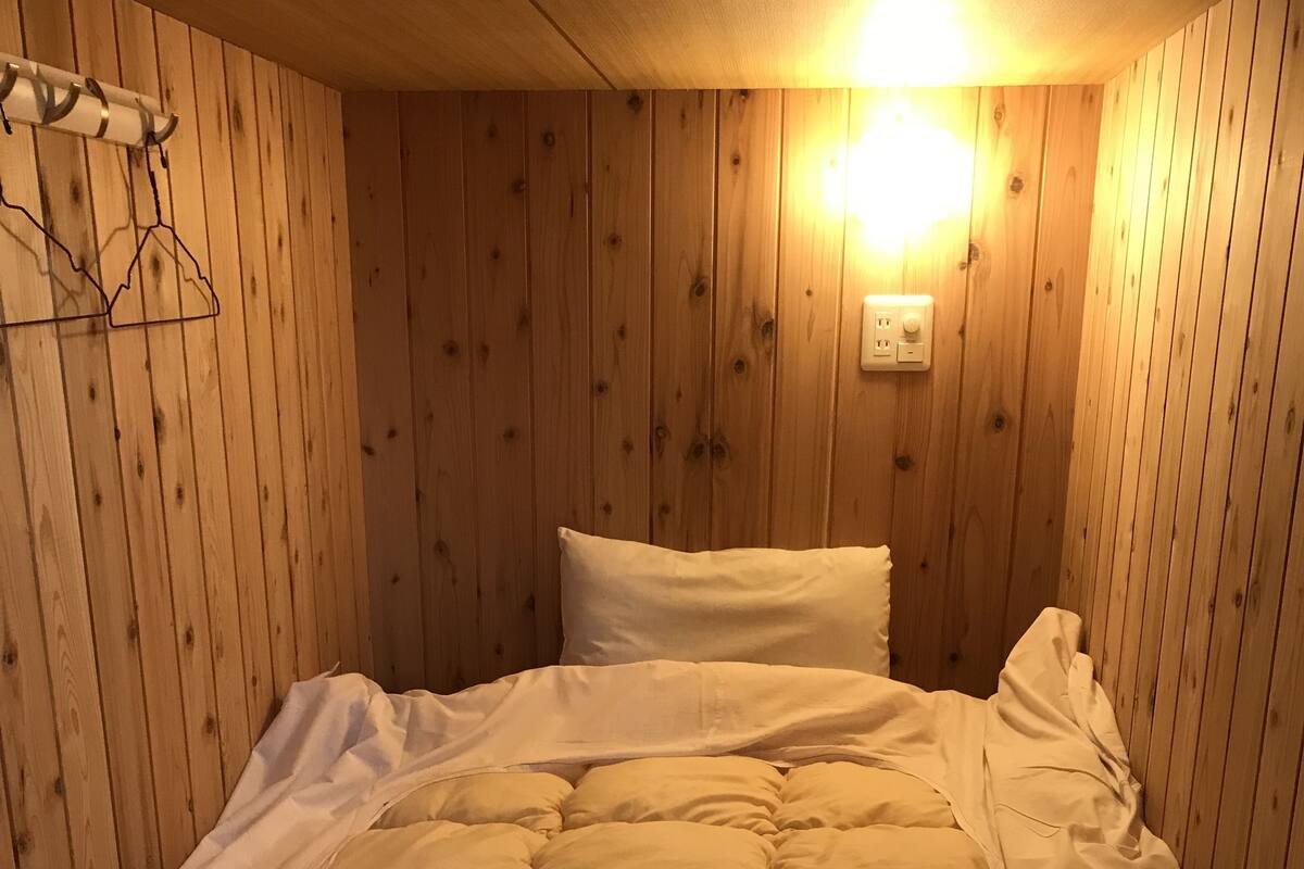 Un lit simple avec une couette matelassée, des murs en bois et un luminaire fixé au mur.