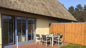 Une terrasse avec une table et des chaises, un toit de chaume et une clôture en bois.