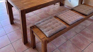 Une table à manger en bois avec des bancs, un téléviseur et des luminaires suspendus dans une pièce dont le sol est recouvert de carreaux.