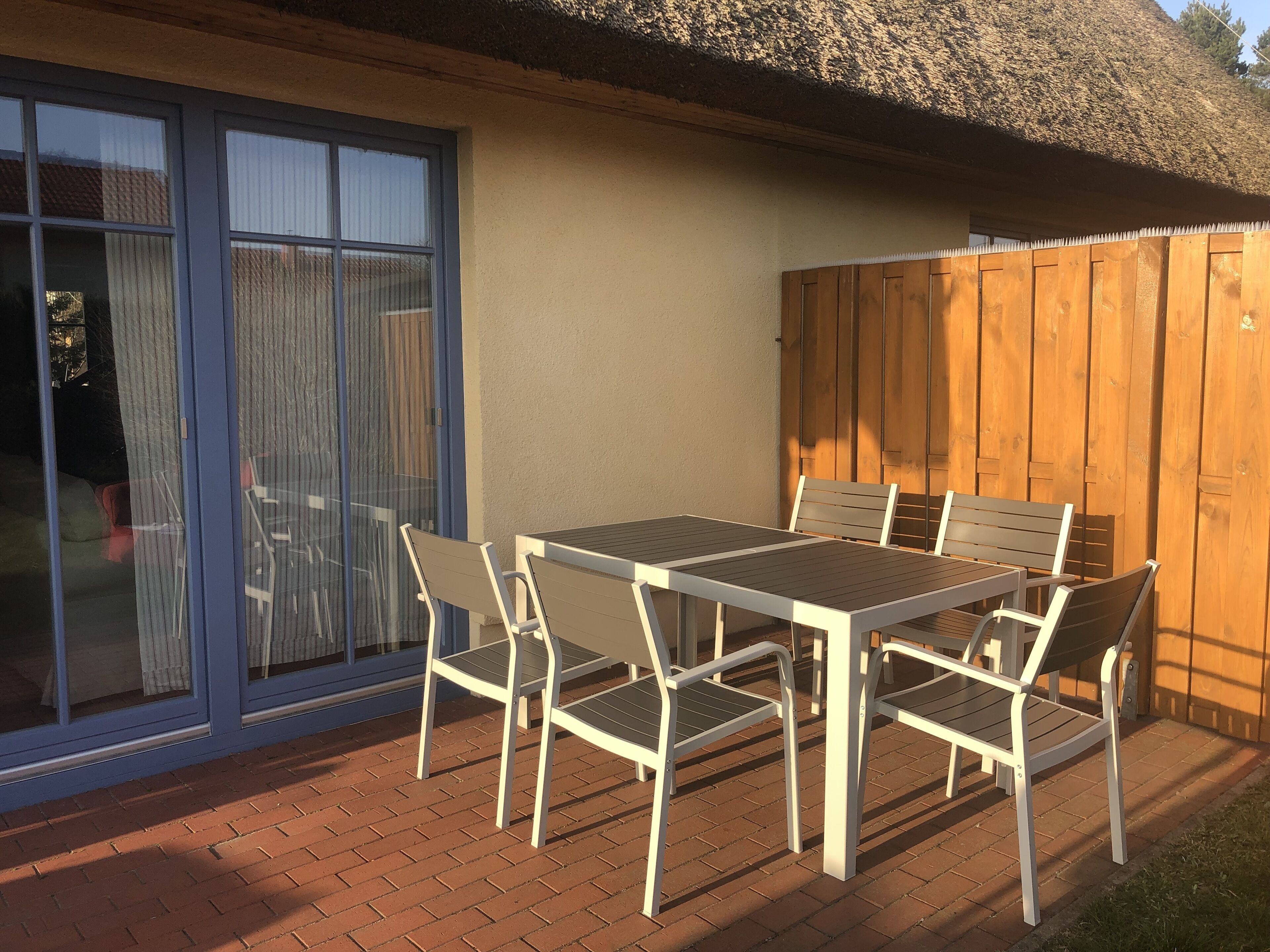 Eine Terrasse mit Tisch und Stühlen, einer Glastür und einem Holzzaun.