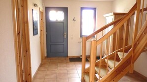 Un couloir avec un escalier en bois, une porte bleue et une fenêtre.
