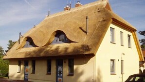 A building with a unique thatched roof and a yellow facade. - Beautiful thatched roof house with south-facing terrace, 2 shower rooms and 2 parking spaces (Prerow)