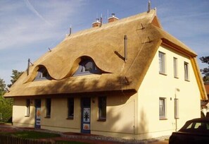 A building with a unique thatched roof and a yellow facade. - Beautiful thatched roof house with south-facing terrace, 2 shower rooms and 2 parking spaces (Prerow)